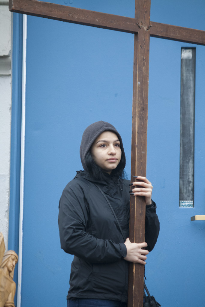 Maria Celeste Lara of St. Monica-St. Augustine Church holds the cross while standing atop steps at one of the stations during the outdoor ecumenical Way of the Cross on Friday, March 25, 2016, in South Boston. (Photo by Susan Doucet)
