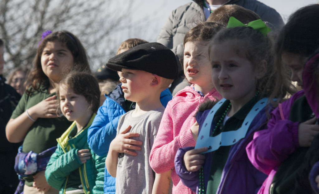 Children stand with their hands on their chests for the pledge of allegiance on Evacuation Day, March 17, 2016. (Photo by Susan Doucet)