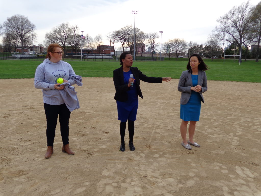 South Boston Girls Softball League President Mariella Collins (left) speaking to the crowd as Sen. Linda Dorcena Forry and Boston City Council President Michelle Wu wait to throw out the first two pitches.